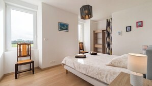Une chambre à coucher comprenant un lit, une chaise, une table de chevet avec une lampe, une fenêtre et une vue sur l’extérieur.