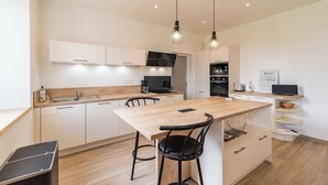 Une cuisine moderne avec des meubles blancs, un îlot central en bois, des chaises noires et des luminaires suspendus.
