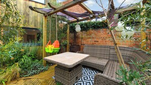 Un espace extérieur accueillant, aménagé avec des meubles en osier, une table et une pergola offrant de l’ombre.