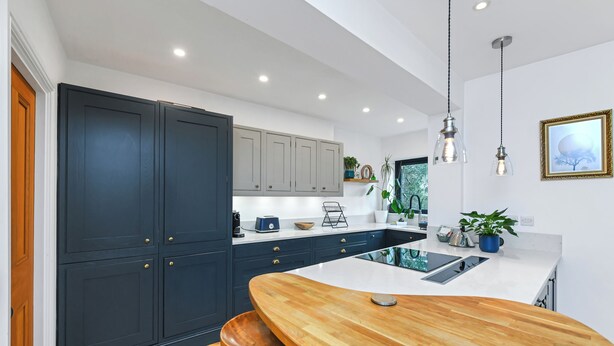 Une cuisine moderne avec des meubles de couleur sombre, un îlot central en bois et des luminaires suspendus.