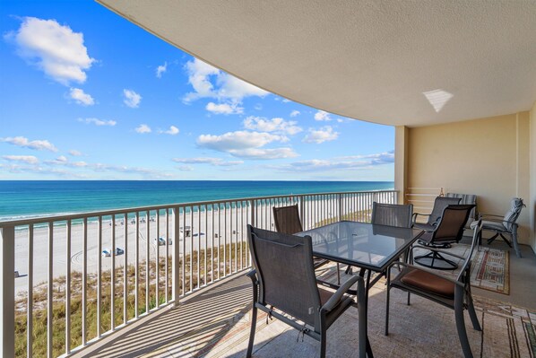 Ein Balkon mit Glastisch und Stühlen mit Blick auf einen Strand und den Ozean.