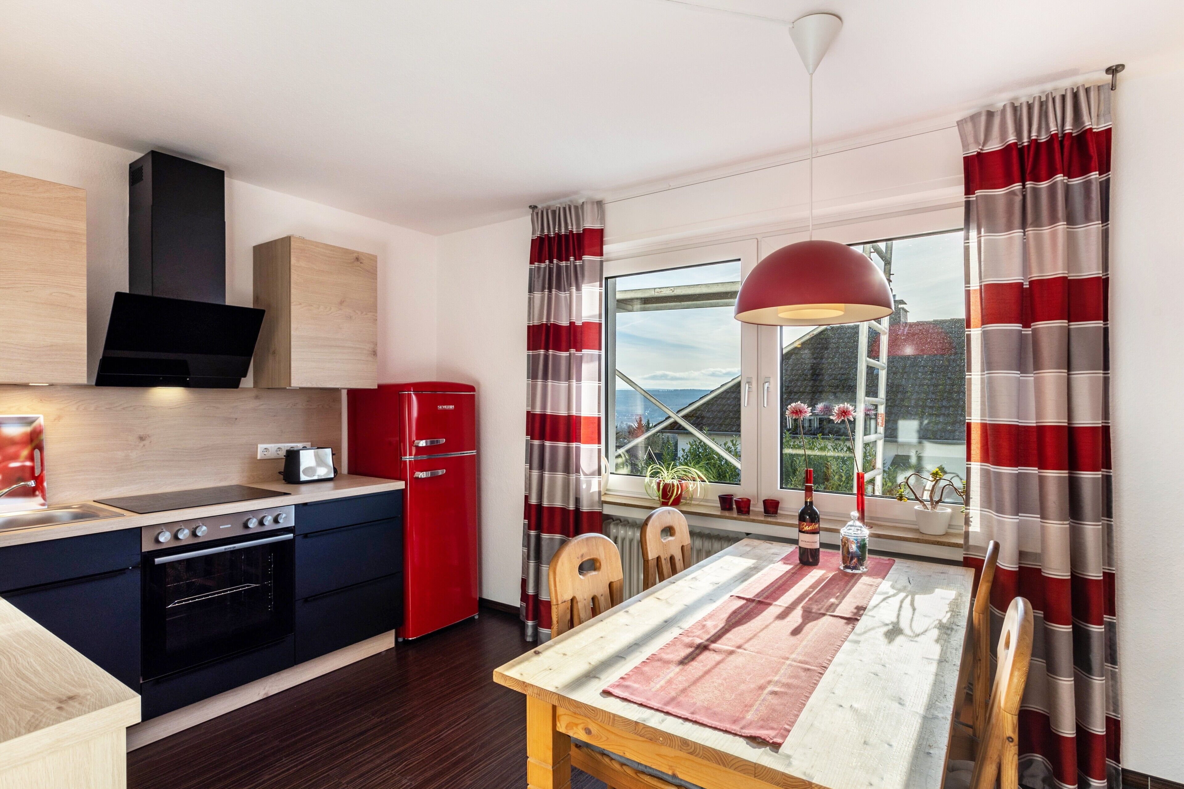 A modern kitchen with a red refrigerator, wooden cabinets, and a dining area with a table and chairs.
