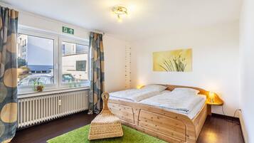 Ein Zimmer mit Bett, einem Vorhangfenster, einem Heizkörper, einem grünen Teppich und einer Wandleuchte.