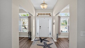 A hallway with a starfish-patterned rug, a chandelier, and a white door.