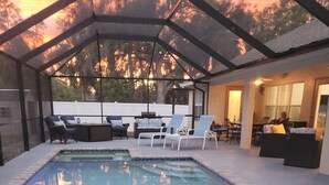 An indoor swimming pool with a glass ceiling, surrounded by lounge chairs and a seating area with a view of trees.