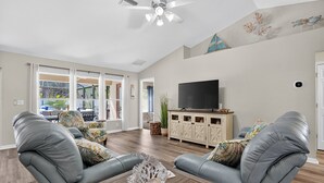 A spacious living room with leather sofas, a flat-screen TV, and a ceiling fan.
