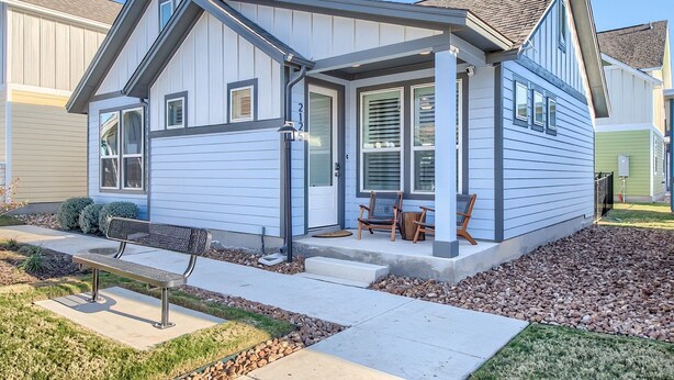 A single-story house with a front porch, a small garden, and a metal bench. - Ot 2125 Creekside Cottage 2 Bedroom Home (New Braunfels)