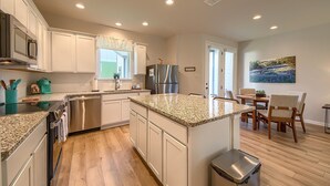 A modern kitchen with white cabinets, granite countertops, a stainless steel refrigerator, and a dining area with a table and chairs. - Ot 2125 Creekside Cottage 2 Bedroom Home (New Braunfels)