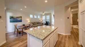 A modern kitchen with a granite countertop, wooden flooring, and a dining area with a table and chairs. - Ot 2125 Creekside Cottage 2 Bedroom Home (New Braunfels)