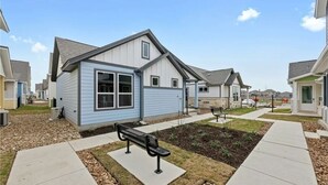 A residential area with houses, a paved walkway, and a bench. - Ot 2125 Creekside Cottage 2 Bedroom Home (New Braunfels)