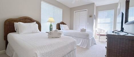 A hotel room with two beds, a ceiling fan, a lamp, and a wicker chair.