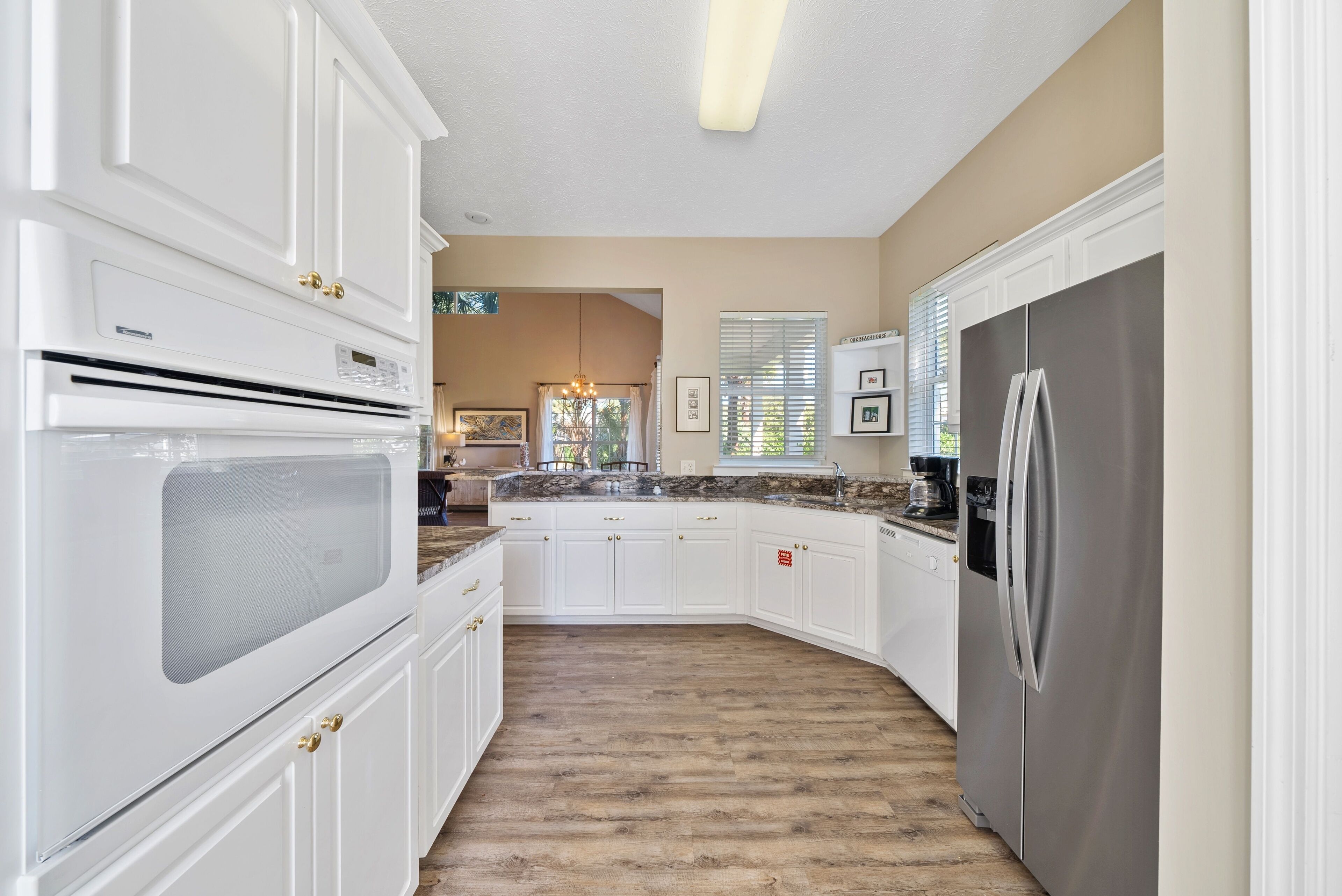 A kitchen with white cabinets, a stainless steel refrigerator, and a wooden floor.