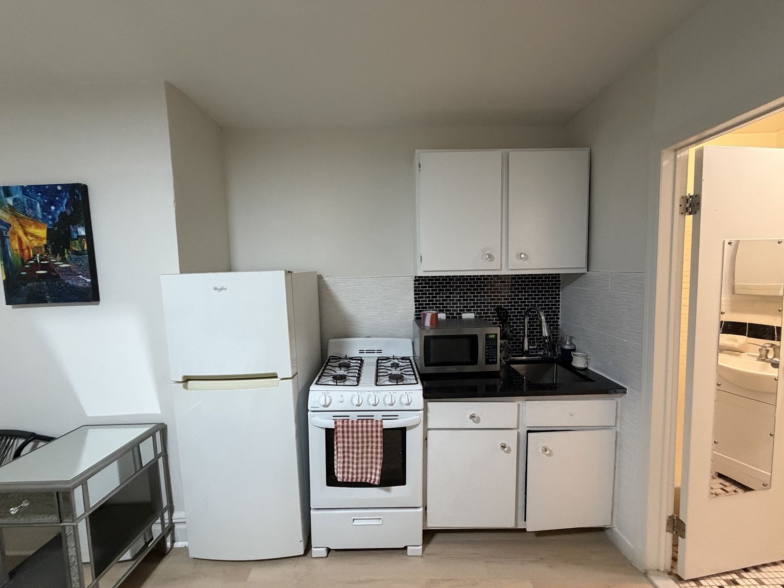 A compact kitchen with white cabinets, a stove, a microwave, and a refrigerator.