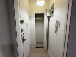 A narrow hallway with a door on the left, a light fixture above, and a phone on the right.