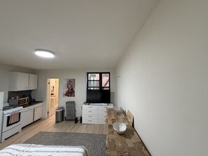 A compact kitchen with white cabinets, a microwave, and a stove. There's a dining area with a table and chairs, and a large window with a view of the outside.