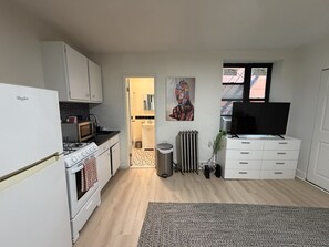Cocina compacta con refrigerador, estufa, microondas y un televisor sobre un mueble.
