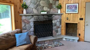 A cozy room with a stone fireplace, wooden walls, a cushioned sofa, and a door with a picture above it. - This beautiful Lodge in the woods is perfect for year round enjoyment! (Allegany)