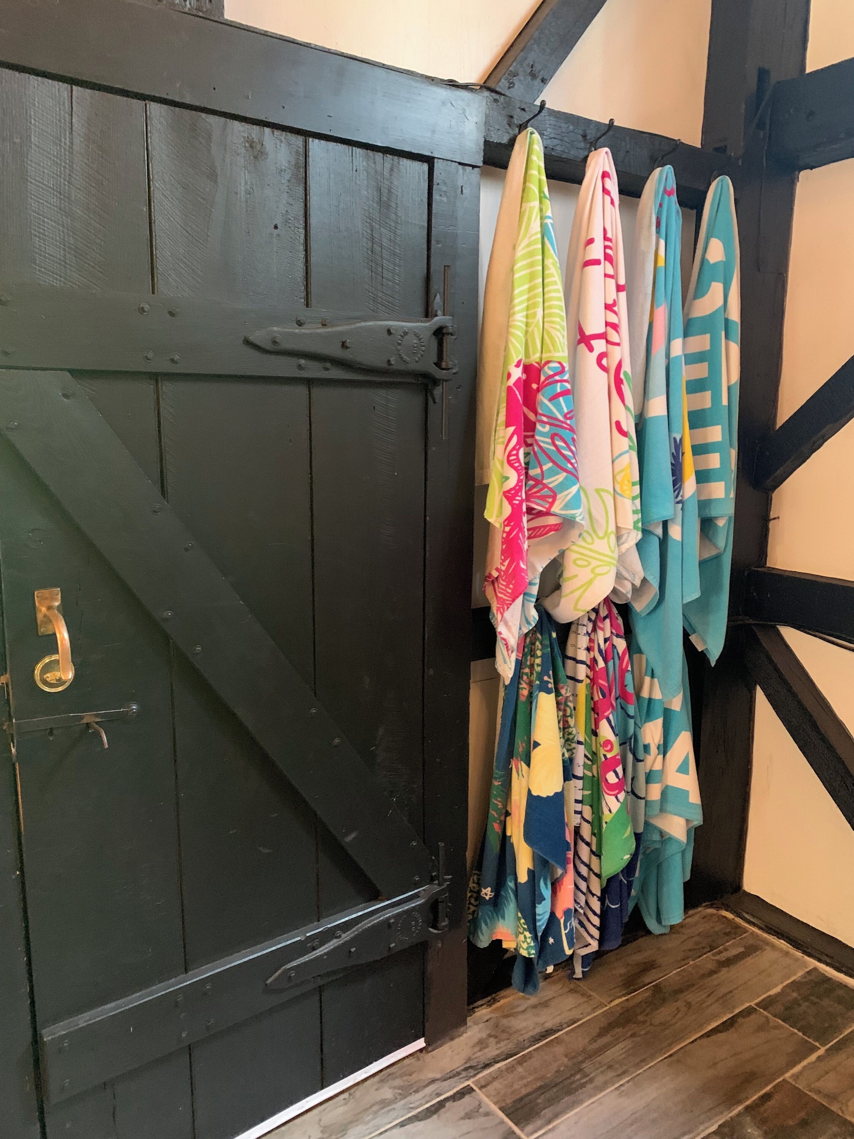 A dark wooden door with a brass handle, a tiled floor, and colorful towels hanging on a rack.