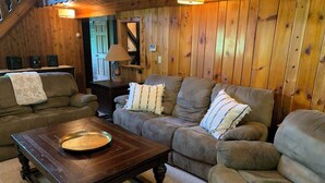 A cozy living room with a wooden interior, a brown sofa set, a coffee table, and a lamp. - This beautiful Lodge in the woods is perfect for year round enjoyment! (Allegany)