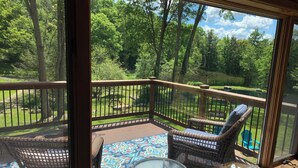 A balcony with wicker chairs and a glass table, overlooking a lush green landscape. - This beautiful Lodge in the woods is perfect for year round enjoyment! (Allegany)