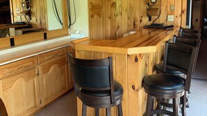 A wooden interior with a bar area, bar stools, a television mounted on the wall, and a wooden cabinet. - This beautiful Lodge in the woods is perfect for year round enjoyment! (Allegany)