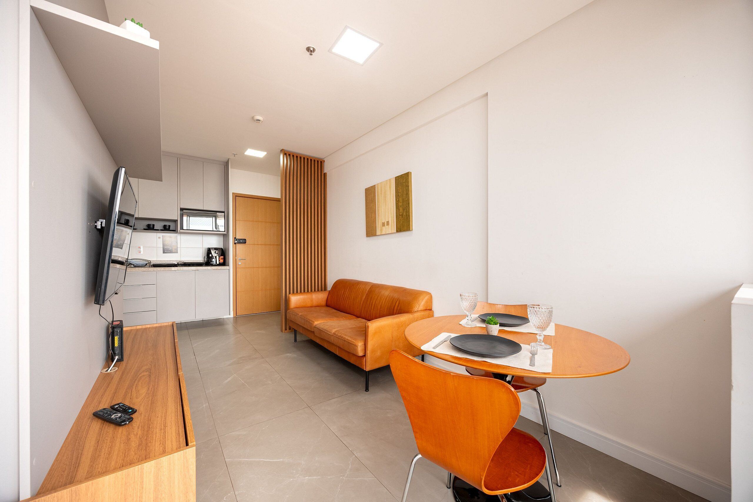 Een moderne keuken met een flatscreen televisie, een eethoek met een houten tafel en oranje stoelen, en een bank.