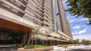 A modern building with multiple floors, large windows, and a covered entrance area with planters. - Apartamento Moderno Premium - Cittyplex  (Osasco)