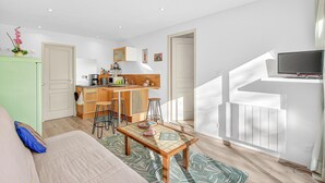 Un espace de vie compact comprenant un coin cuisine, un espace repas avec des tabourets, un canapé et un téléviseur fixé au mur.