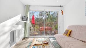 Un salon moderne avec un canapé, une porte vitrée donnant sur un espace extérieur, un radiateur et un téléviseur posé sur une étagère.