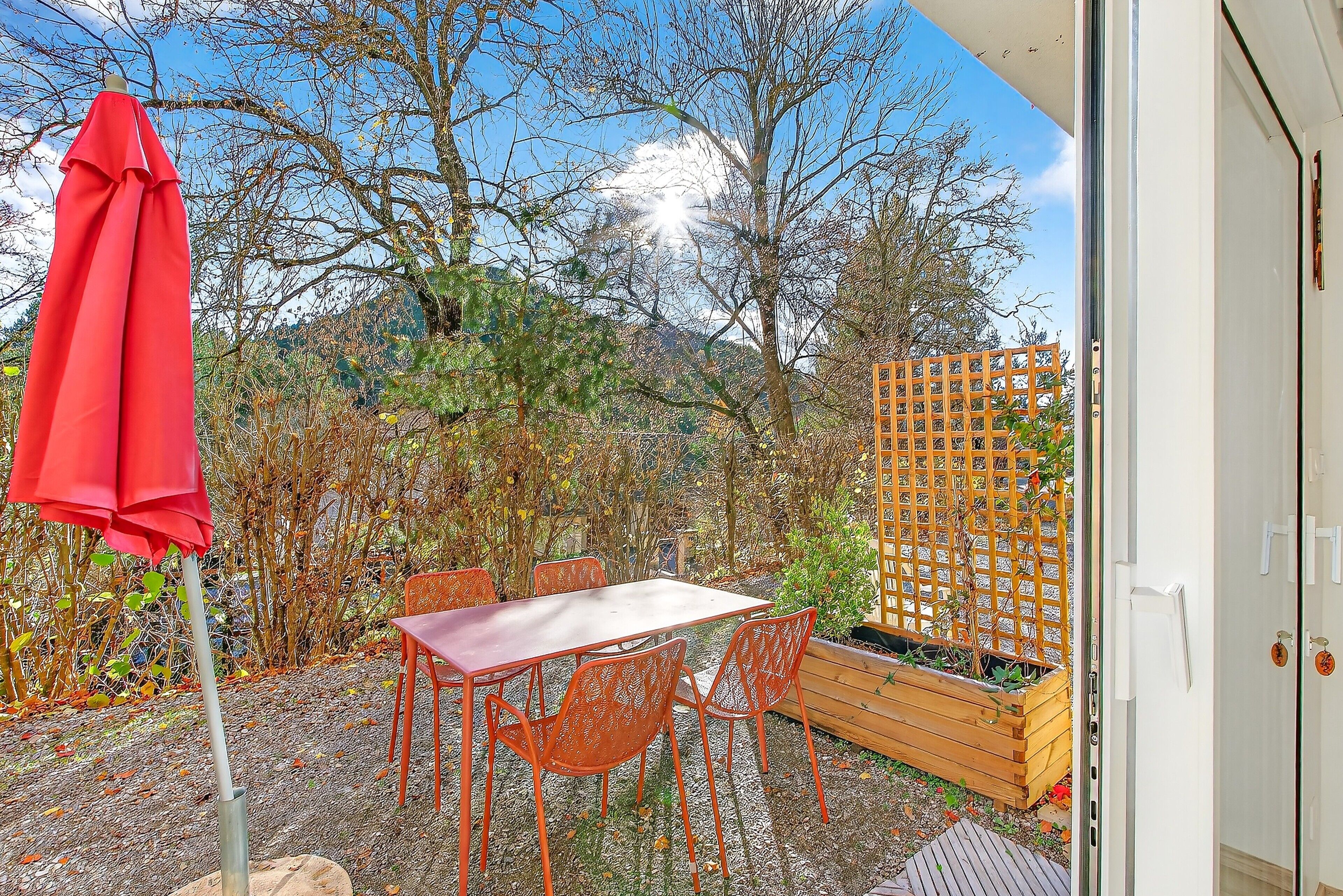A patio with a table and chairs, a red umbrella, and a wooden fence.