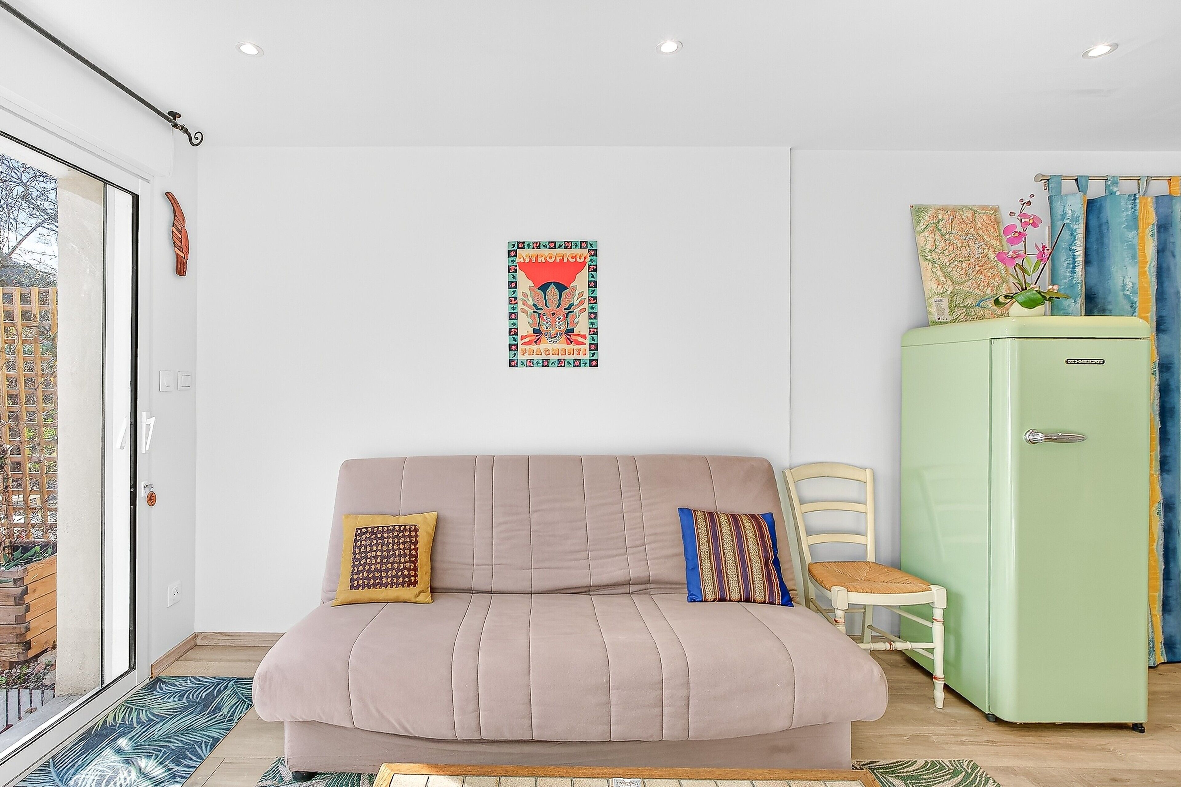 A modern living room with a sofa, a green refrigerator, and a window with a view of a building.