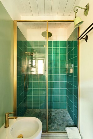 Une salle de bain avec une douche à parois de verre, un lavabo blanc et un mur recouvert de carreaux verts.