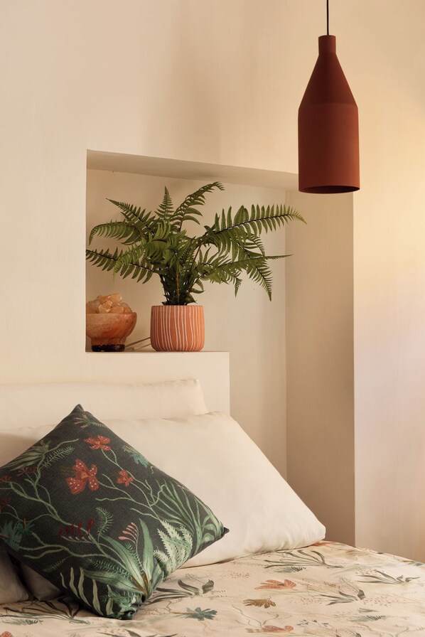 A bedroom with a bed, a hanging pendant light, a potted plant, and a decorative pillow.