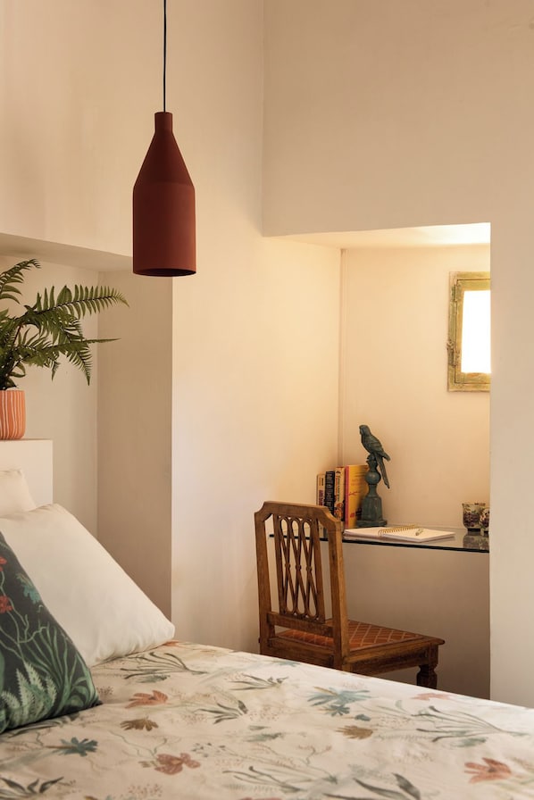 A bedroom with a bed, a chair, a desk, a hanging light, and a plant.