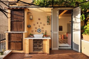 A small outdoor kitchen area with a sink, potted plants, and a decorative wall.