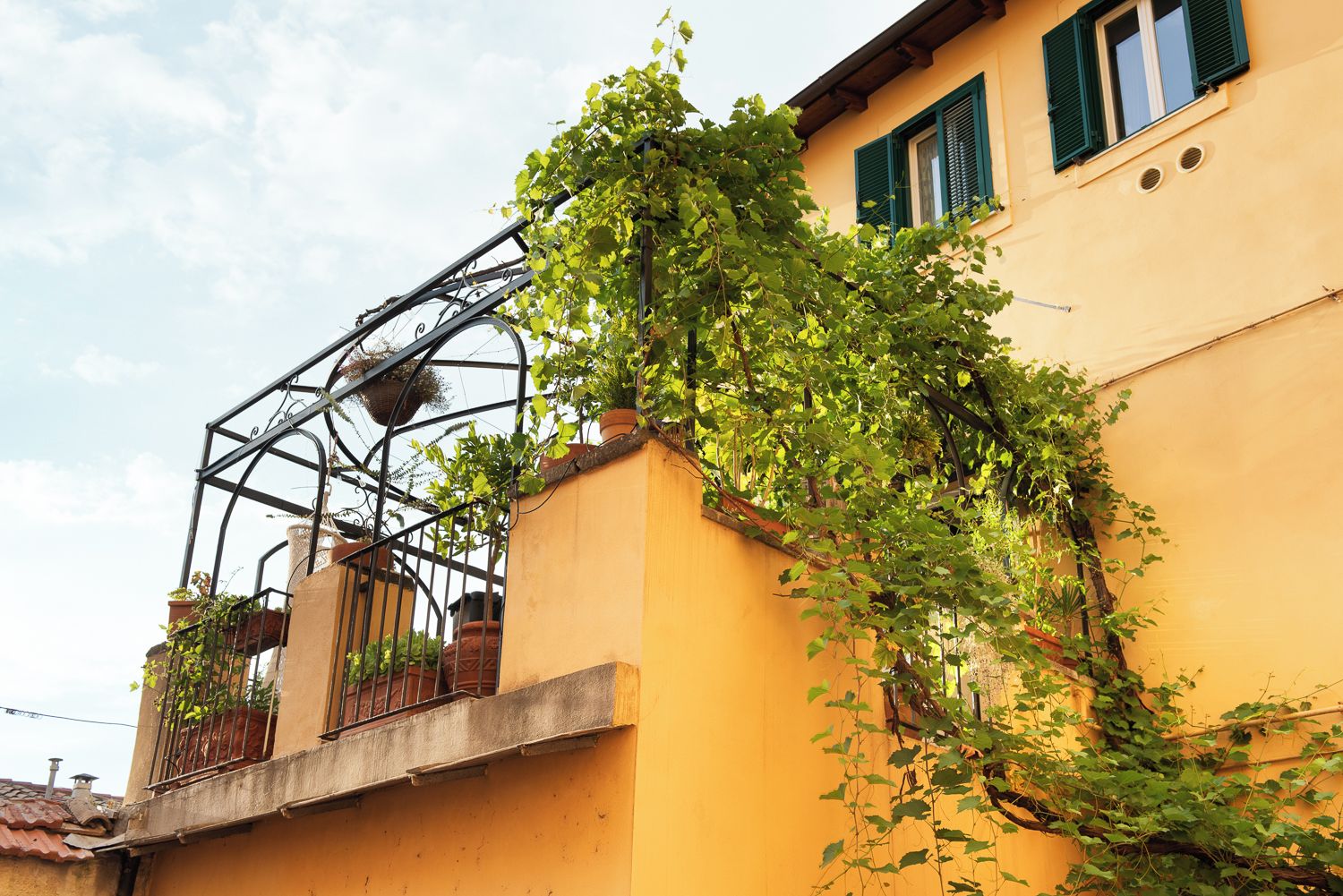 A yellow building with a metal balcony structure and green shutters.