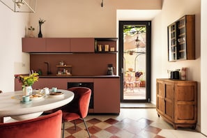 A modern kitchen with a dining area, featuring a round table, red chairs, and a view of an outdoor patio.