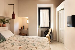 A bedroom with a bed, a chair, a window with curtains, a radiator, and a television on the wall. - La Voliera di Bacco – Vacation Home in Frascati (Frascati)