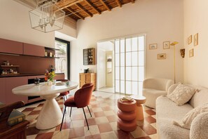 A spacious living area with a round dining table, a sofa, and a large window providing natural light.