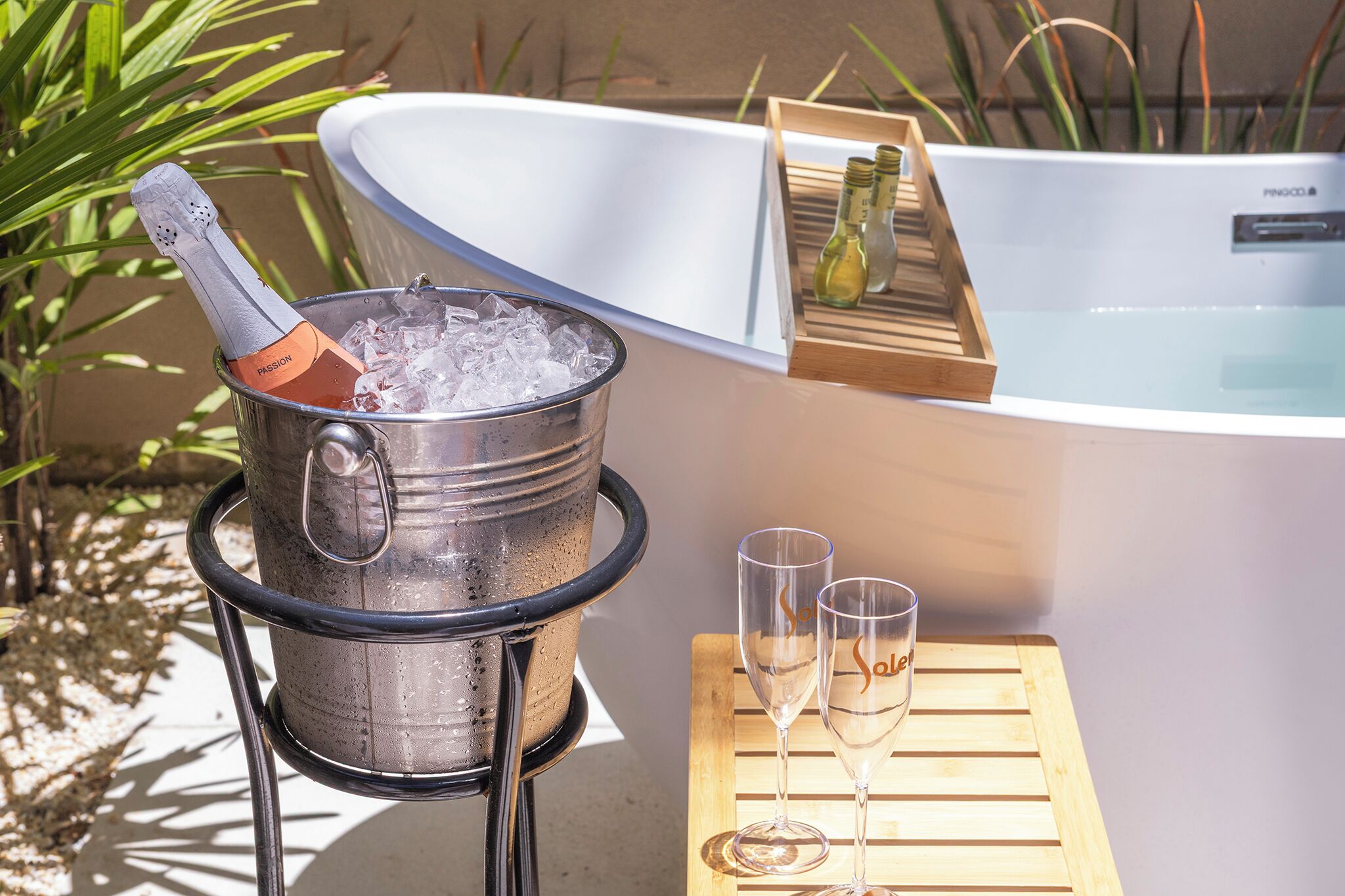 Jacuzzi con un recipiente de madera que sostiene dos vasos y un contenedor metálico con una botella.