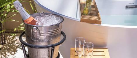 Jacuzzi con un recipiente de madera que sostiene dos vasos y un contenedor metálico con una botella.