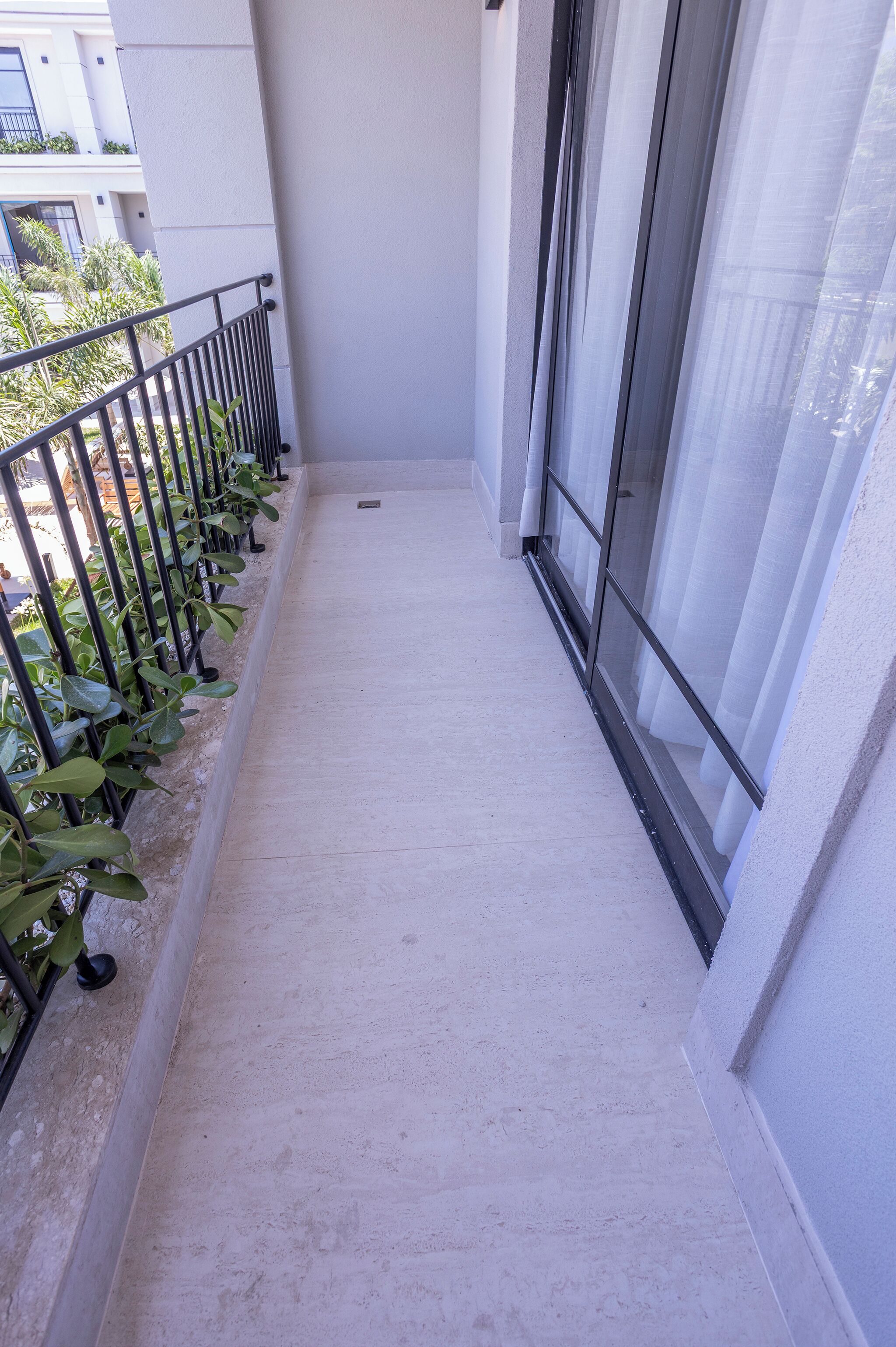 A narrow balcony with a metal railing, a concrete floor, and a view of a building with windows and a door.