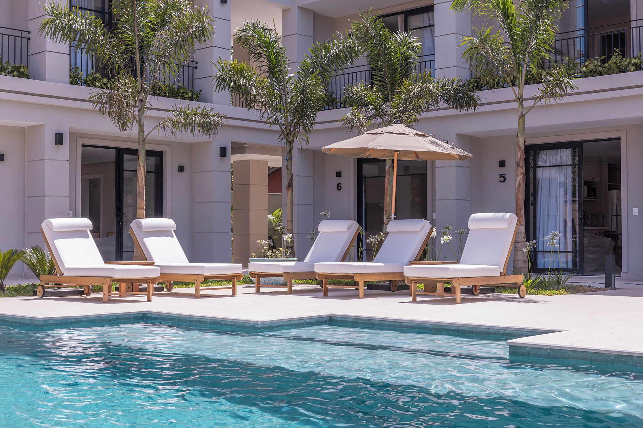 A poolside area with lounge chairs and an umbrella, surrounded by a building with balconies and a pool.