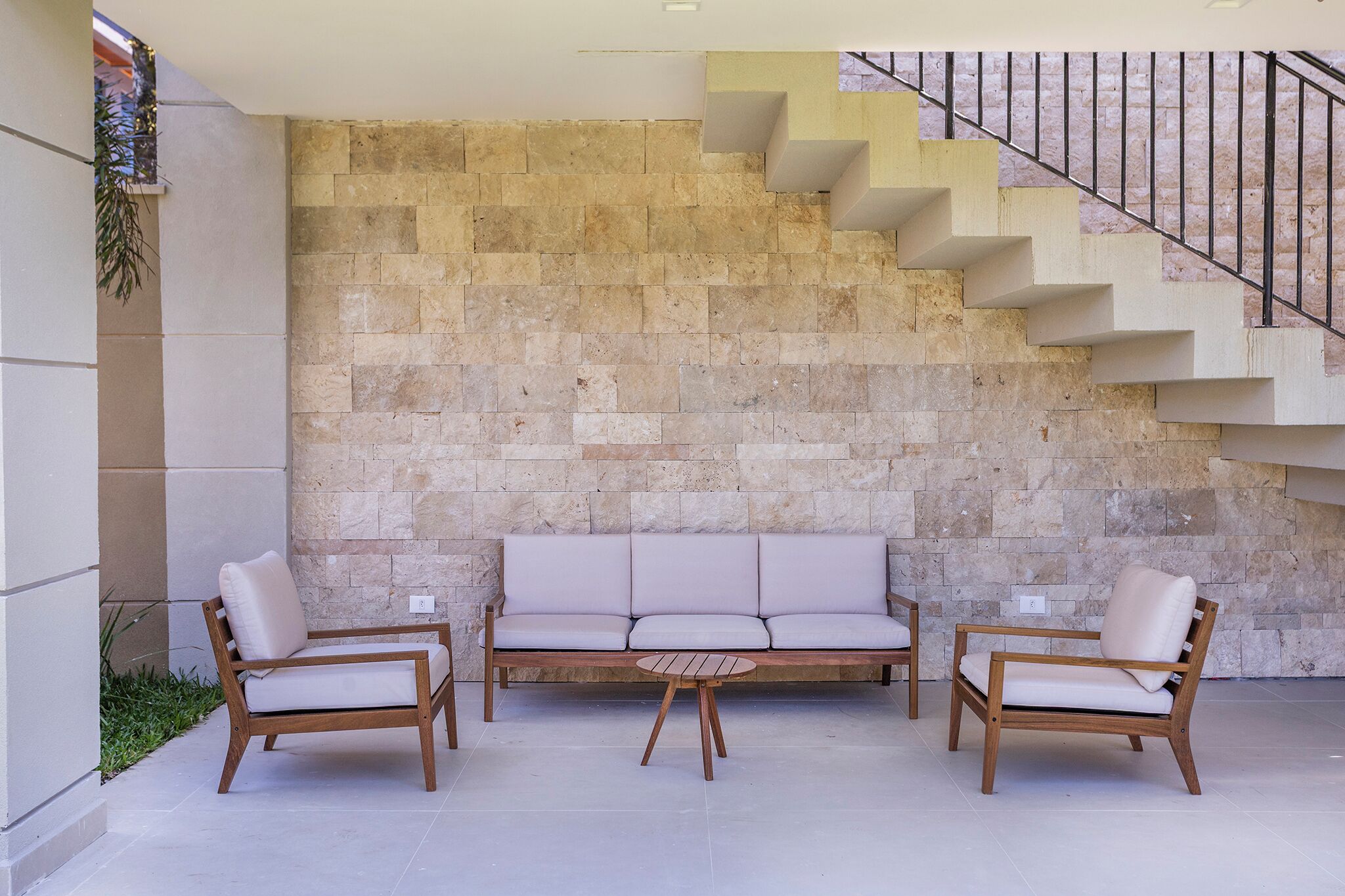 A modern outdoor seating area with a stone wall backdrop, a wooden bench, and two chairs.