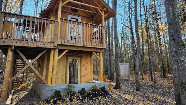 A wooden cabin with a balcony, surrounded by trees. - The Rustic Treehouse Hideaway-cozy treehouse retreat in Northern Ontario (Corbeil)