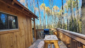A wooden deck with a picnic table and a grill, surrounded by trees. - The Rustic Treehouse Hideaway-cozy treehouse retreat in Northern Ontario (Corbeil)
