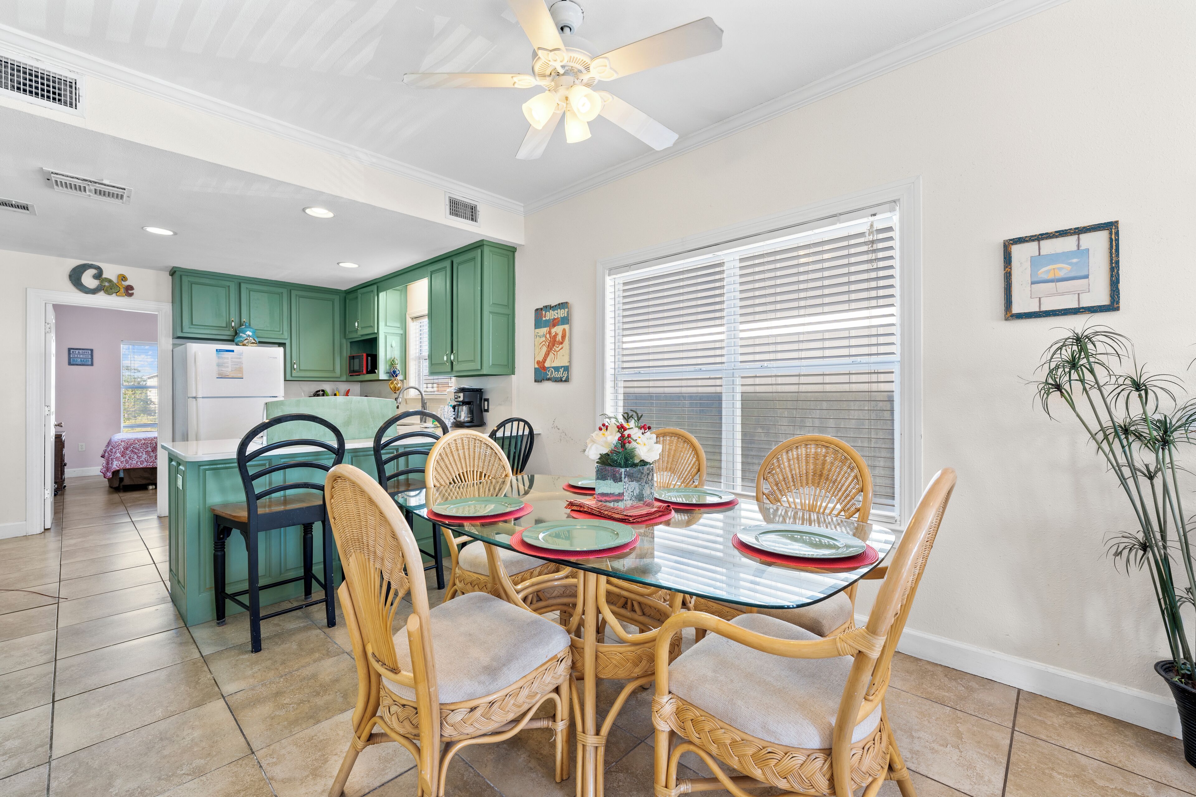 A dining area with a glass table, wicker chairs, and a ceiling fan.