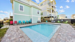 A swimming pool with a brick deck, surrounded by colorful chairs and a multi-story building with balconies. - Sea Watch Unit A (Gulf Shores)