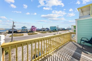 Eine Holzterrasse mit Blick auf einen Strand und farbenfrohe Häuser im Hintergrund.