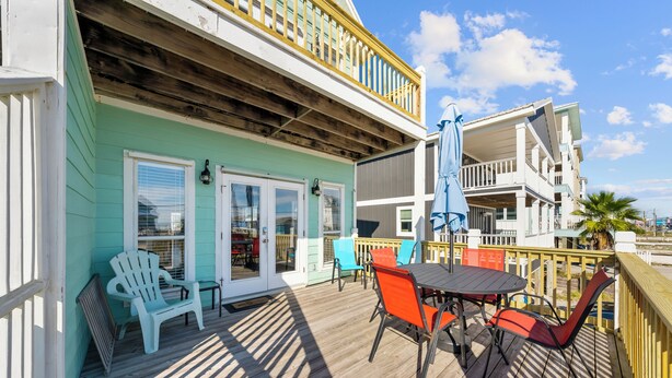 A wooden deck with a table and chairs, a covered area with a railing, and a building with a balcony. - Sea Watch Unit A (Gulf Shores)